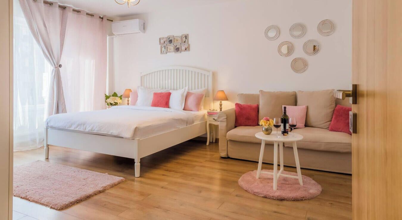 A bedroom with a bed, a sofa, a small round table with drinks, and a wall with decorative items.