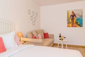 Ein Hotelzimmer mit Bett, einer Couch, einem kleinen Tisch mit Flasche und Gläsern sowie einem Gemälde an der Wand.