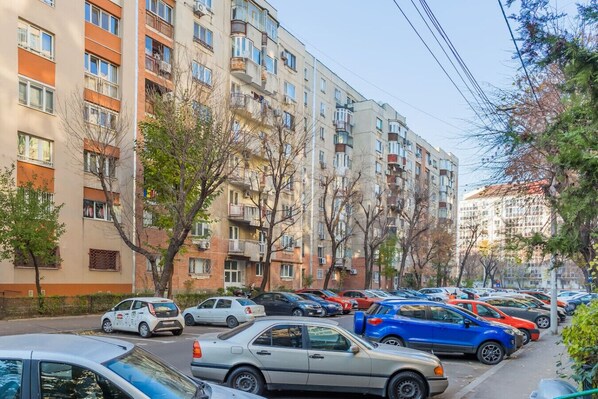 Un edificio residencial de varios pisos con balcones, coches aparcados y árboles.