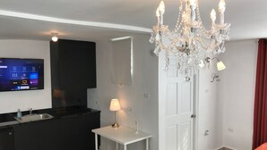 Een hotelkamer met een aan de muur bevestigde televisie, een kroonluchter, een bureau met een lamp, een stoel en een bed.