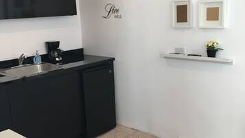 A modern kitchen with a black countertop, a white sink, and a black refrigerator. There is a white shelf with a potted plant and a framed picture.