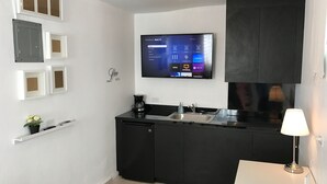 Een compacte keuken met een zwart aanrecht, een ingebouwd spoelbakje, een koffiezetapparaat en een aan de muur bevestigde televisie waarop een menu wordt weergegeven.