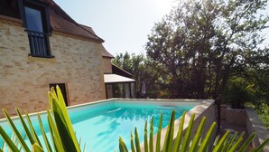 Une piscine entourée d’un bâtiment en pierre et d ’une végétation luxuriante.