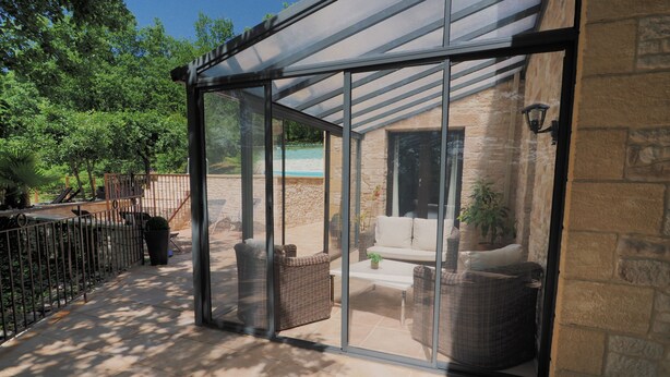 Un patio vitré, aménagé avec des meubles en osier et doté d’un mur en pierre.