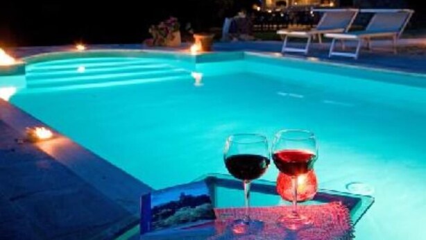 Una piscina con sillas de descanso y velas, sugiriendo un ambiente relajante para la noche.