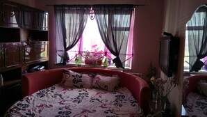 A bedroom with a bed, a TV, a bookshelf, and a window with curtains. - Comfortable apartment near the International Exhibition Center and  metro. (Київ)