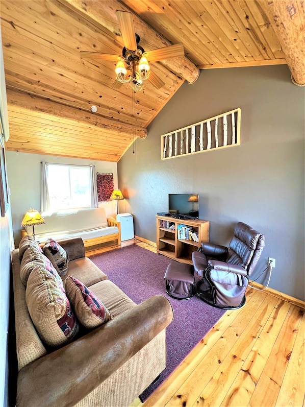 A cozy living room with a wooden ceiling, a sofa, a recliner, a TV stand, and a bookshelf. - #4 Elk Cabin at Ponderosa Place (Custer)