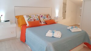Un letto rifatto con cura, con una coperta blu e arancione, due cuscini arancioni e una testiera decorata con motivi floreali.