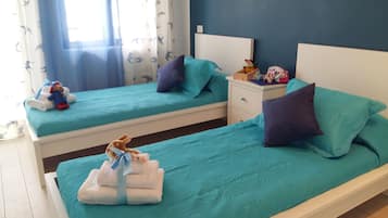 Two single beds with matching bedspreads and pillows, a nightstand, and a window with sheer curtains.