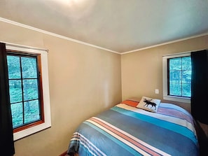 Un dormitorio con cama, dos ventanas y una lámpara en el techo.