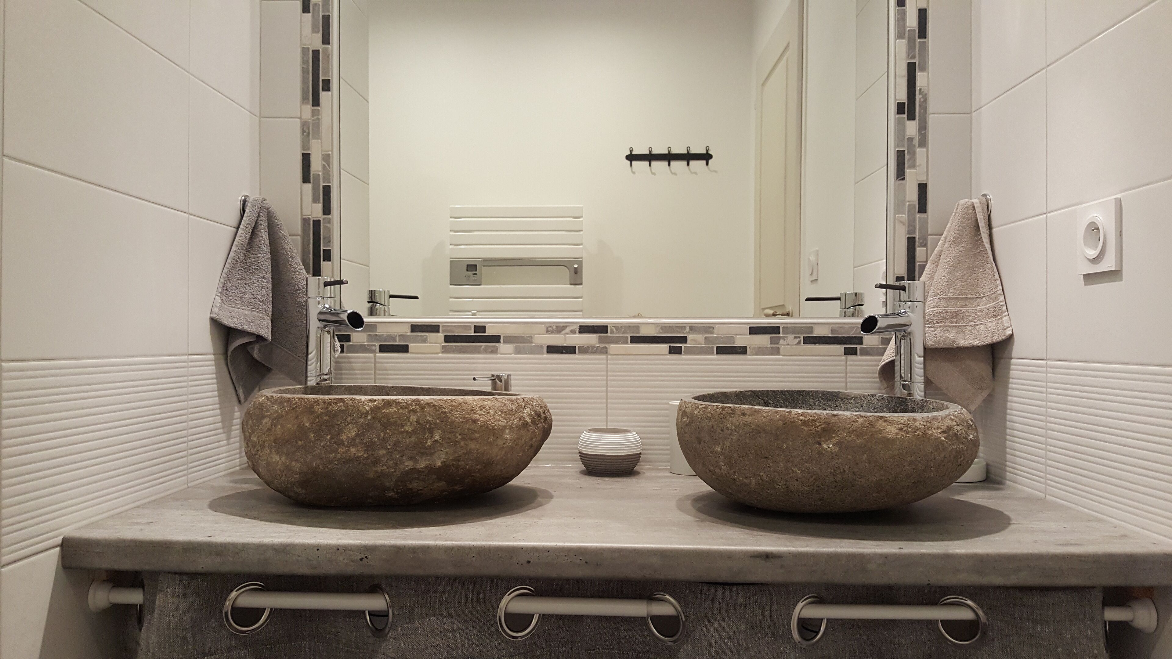 A bathroom with two large stone sinks, a mirror, and a tiled backsplash.