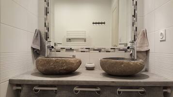 A bathroom with two large stone sinks, a mirror, and a tiled backsplash.