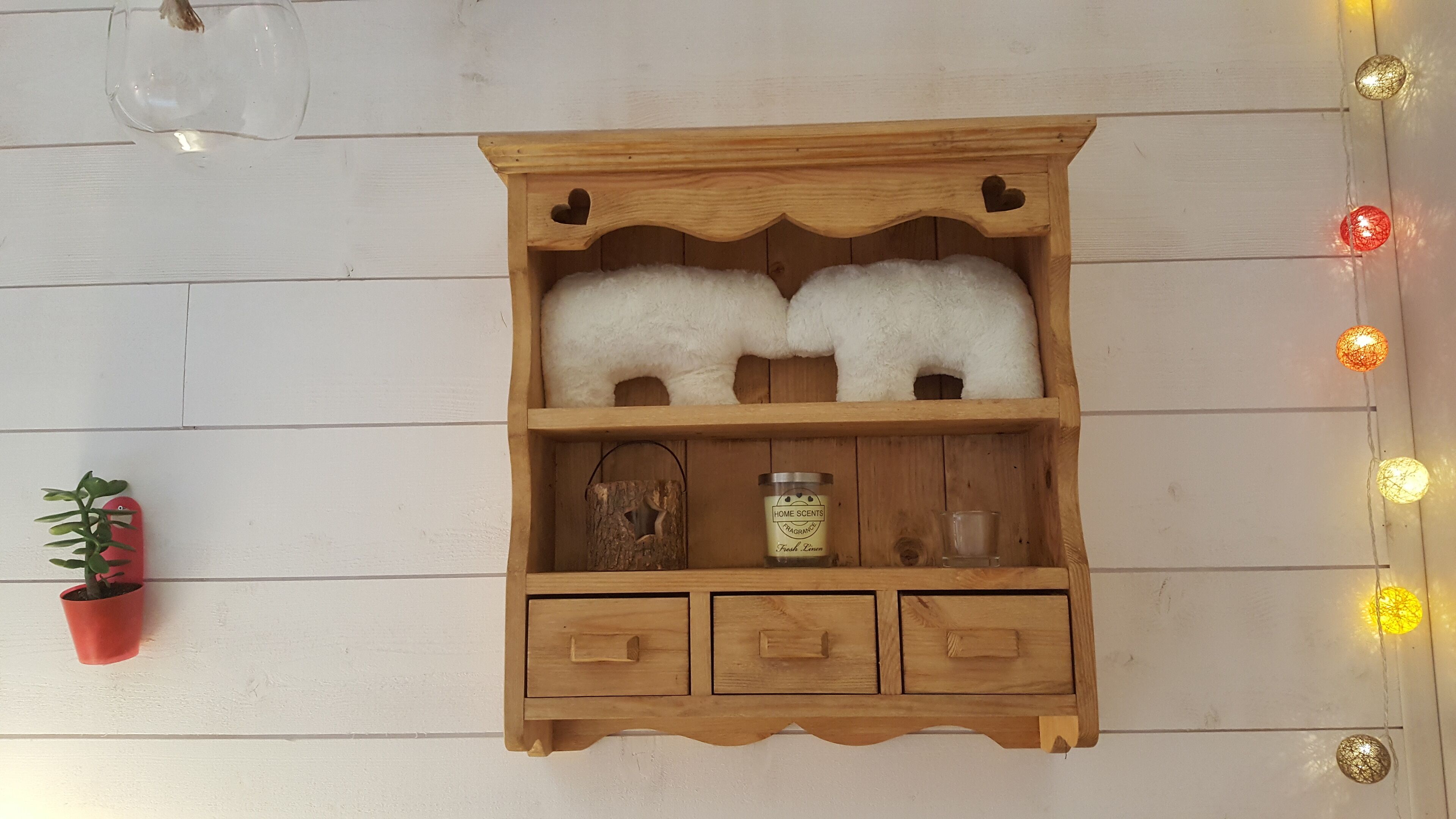 Un meuble en bois sur lequel reposent deux objets blancs et duveteux, une petite plante en pot, une bougie et un verre.