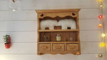 A wooden cabinet with two white fluffy objects, a small potted plant, a candle, and a glass.