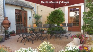 An outdoor patio with a wooden table and chairs, surrounded by potted plants and flowers.