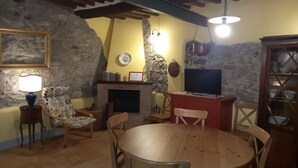 Een gezellige woonkamer met een stenen muur, een open haard, een televisie en een eettafel met stoelen.