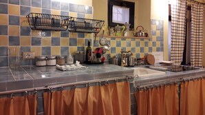 Een keuken met een betegelde spatwand, een hangend metalen rek, en diverse keukenbenodigdheden op het aanrecht.