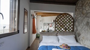 A bedroom with a large bed, a window, a stone wall, and a view of the sea. - Apartment in studio villa called Vulcano sleeps 2 (REITANO)
