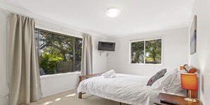 Una camera da letto con un letto, una TV a muro, una finestra con tende e una lampada su un comodino.