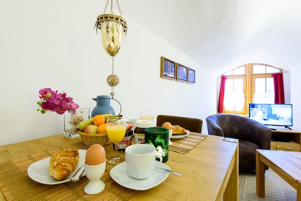 A breakfast setup with a table, chairs, a coffee pot, fruit, eggs, and a television in the background.