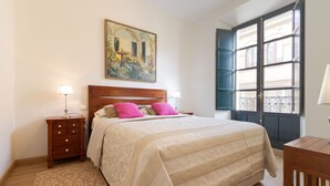 Une chambre à coucher avec un lit, une table de chevet, une lampe, un tableau et une fenêtre avec des volets.