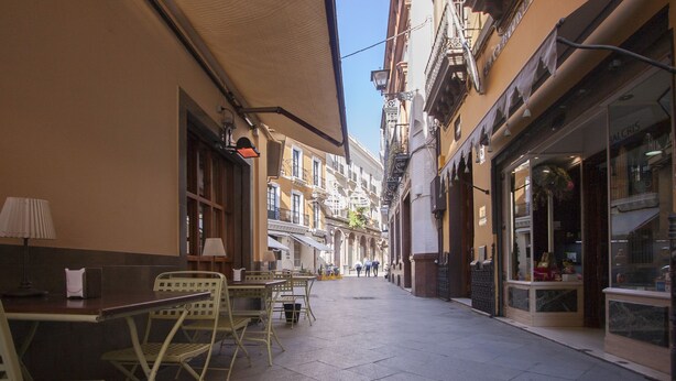 Une rue étroite avec des tables en terrasse, des bâtiments de chaque côté et un ciel dégagé.