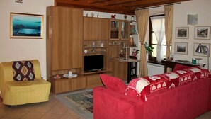 Ein gemütliches Wohnzimmer mit einem Holz-TV-Schrank, einem roten Sofa, einem gelben Sessel und einem Bücherregal.