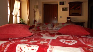 Ein Schlafzimmer mit einem großen Bett, zwei roten Kissen, einer Holzbalkendecke, einer Tür und einem kleinen Tisch mit einer Lampe.