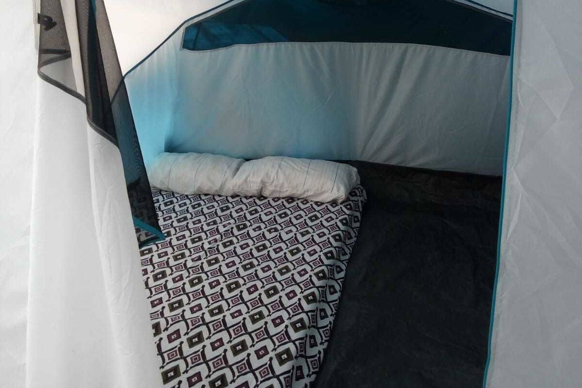 Une tente avec un lit à l’intérieur, agrémentée d’une couverture à motifs et de coussins.