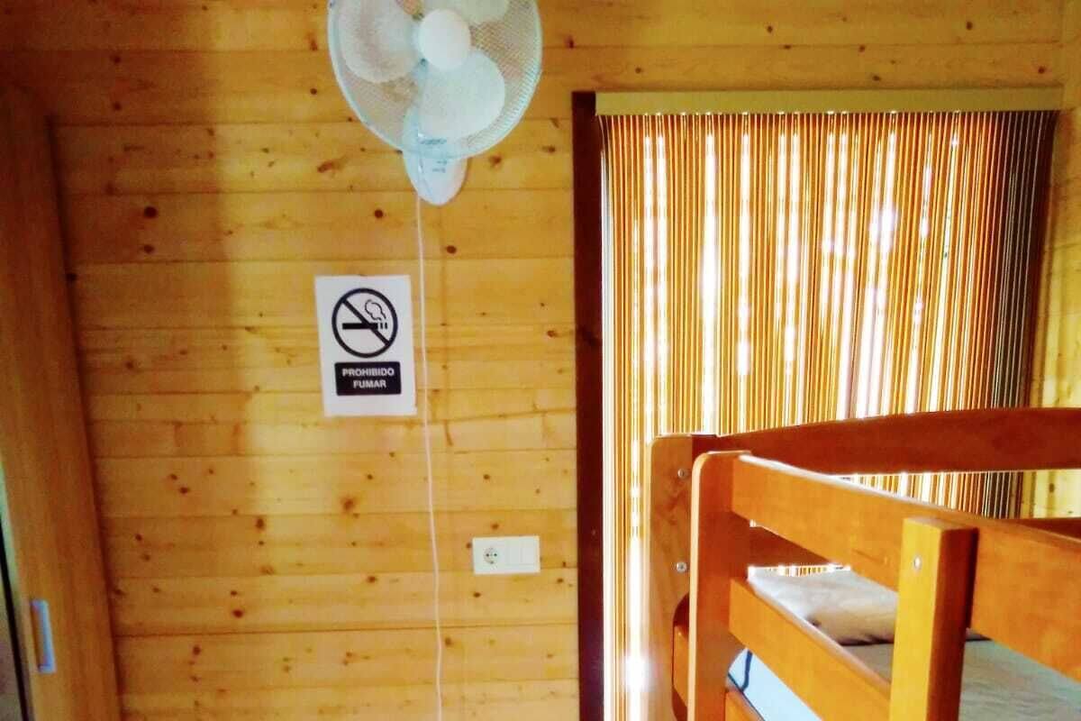 Une pièce en bois avec un lit superposé, un ventilateur de plafond et un rideau.