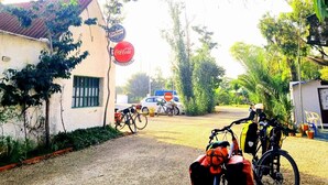 A gravel driveway with bicycles parked on the side, a building with a Coca-Cola sign, and a parked car in the background. - Camping la Naranja (Gandia)