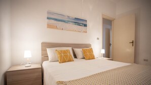 A bedroom with a bed, two bedside tables, a nightstand, a door, and a wall-mounted artwork of a beach scene. - Apartment for rent with terrace (TL66A) (Torre Lapillo)