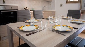 A dining table set with plates, glasses, and cutlery in a modern kitchen with grey chairs and a built-in oven. - Apartment for rent with terrace (TL66A) (Torre Lapillo)