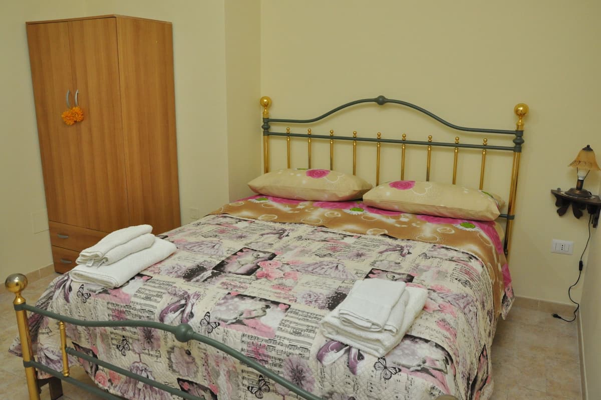 A neatly made bed with floral bedding, a wooden wardrobe, and a bedside lamp.