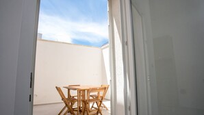 Eine offene Tür, die auf eine Terrasse mit einem Holztisch und Stühlen führt.