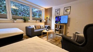A modern living room with a sofa, a small round table, a TV, and a bookshelf. - 3 stars: Apartment on the ground floor, also suitable for wheelchair users (Hamburg)