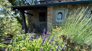 Ein rustikales Steinhaus mit einer Veranda, umgeben von üppiger Vegetation und blühenden Pflanzen.