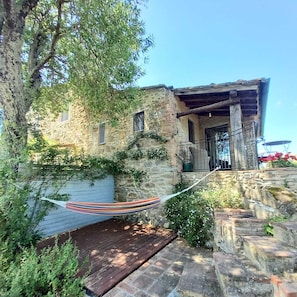 A stone building with a wooden porch, a hammock, and a wooden deck. - Studio in Tuscan farmhouse with views and pool (casole d'elsa)