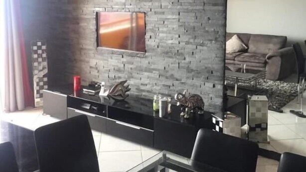 Una sala de estar moderna con pared de ladrillo, un televisor de pantalla plana, un comedor con mesa de vidrio y un sofá.