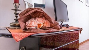 A room with a television on a stand, a decorative lamp, and a patterned tablecloth.