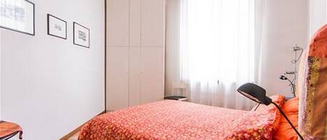 Un dormitorio con cama, mesita de noche, lámpara y armario.