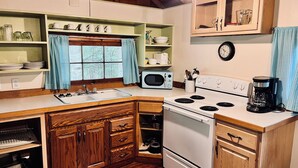 A compact kitchen with wooden cabinets, a white stove, a microwave, and a coffee maker.