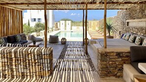 An outdoor lounge area with a pool, stone walls, and wooden furniture. - Seaside Naxos • 2 Villas • 7 Bedrooms / 7 Bath • Sleeps 18 @ Plaka Baech (Naxos)
