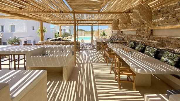 An outdoor seating area with a pool in the background, featuring a wooden pergola and stone walls. - Seaside Naxos • 2 Villas • 7 Bedrooms / 7 Bath • Sleeps 18 @ Plaka Baech (Naxos)