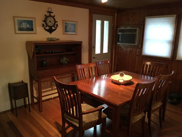 Uma sala de jantar com uma mesa e cadeiras de madeira, um armário de madeira e duas imagens emolduradas na parede.