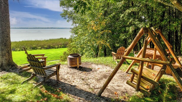 Un conjunto de columpios de madera y sillas Adirondack en un parque con vista al lago.