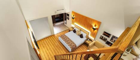 A bedroom with a bed, bedside table, and a nightstand. There is a wooden staircase leading to another room.