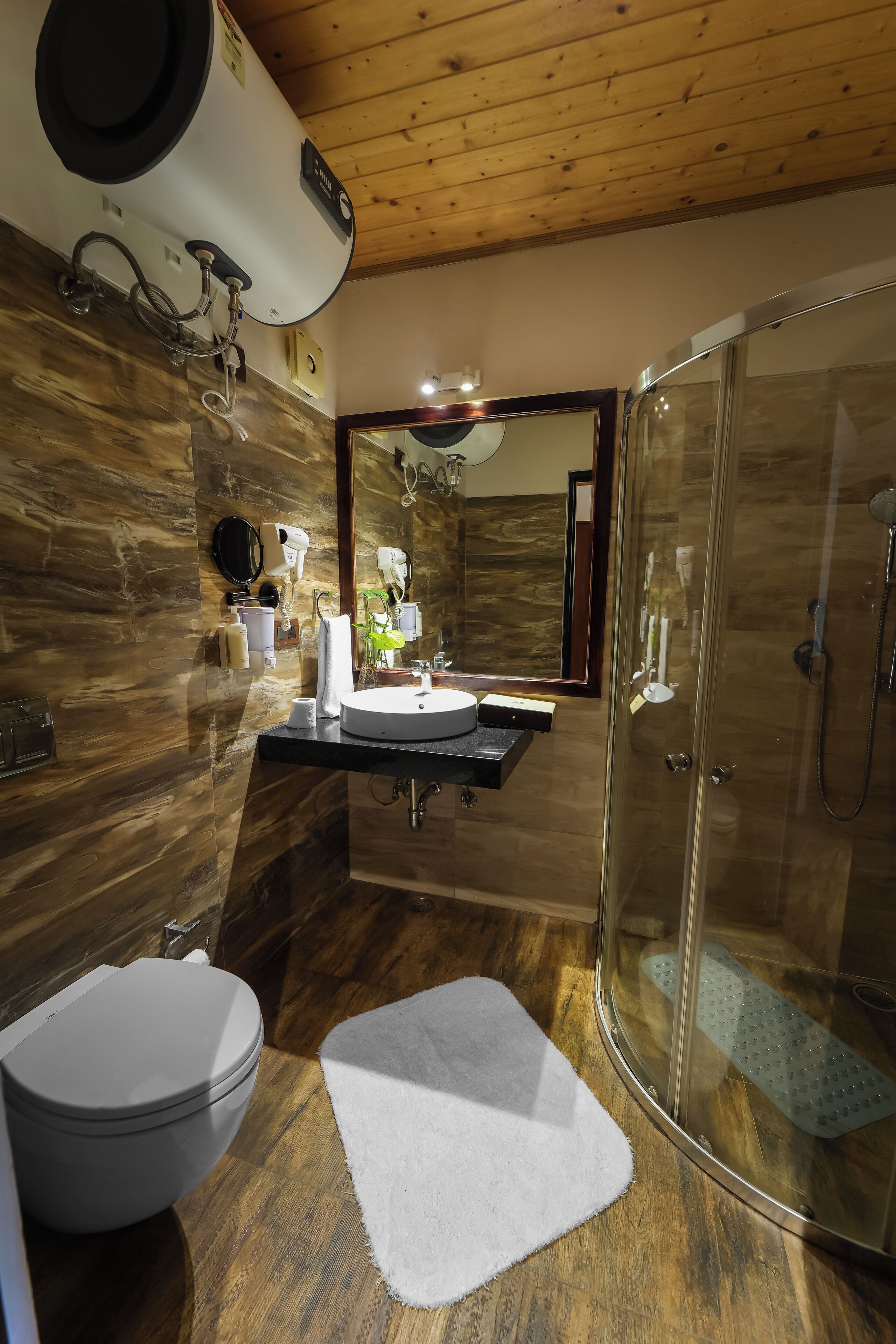 A modern bathroom with a wooden ceiling, a glass-enclosed shower, a sink with a mirror, and a toilet.