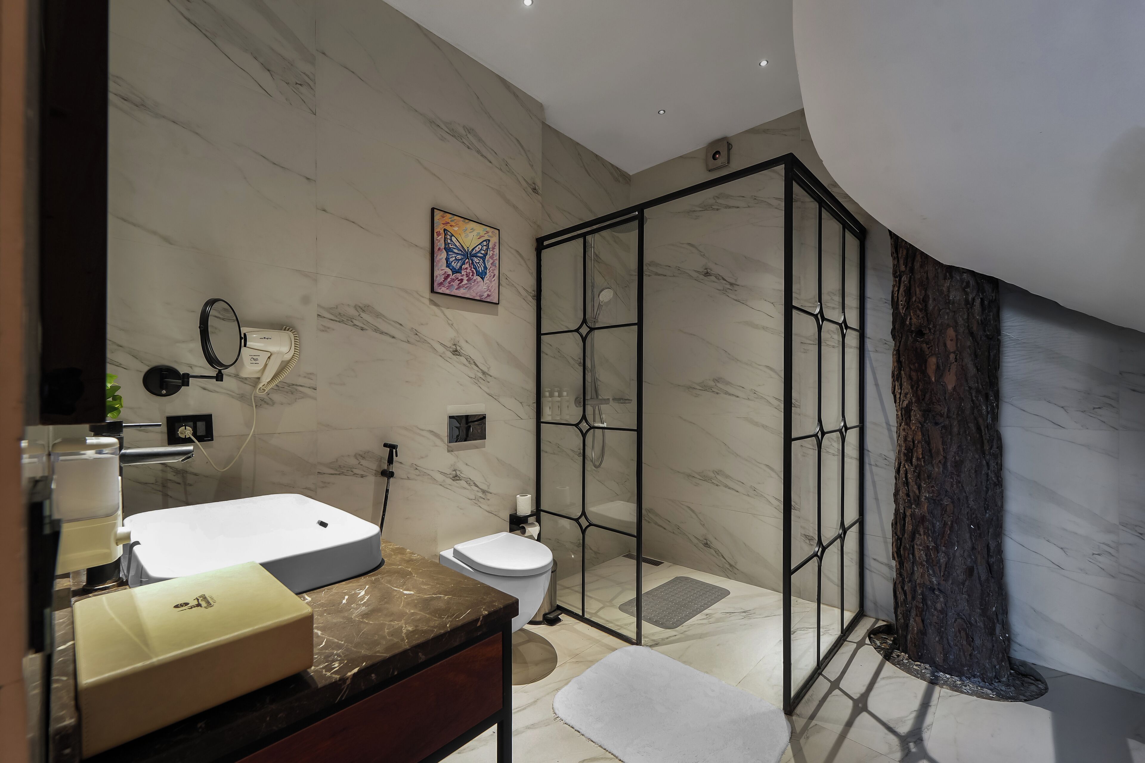 A modern bathroom with a marble floor, a glass shower enclosure, a white sink, and a toilet.