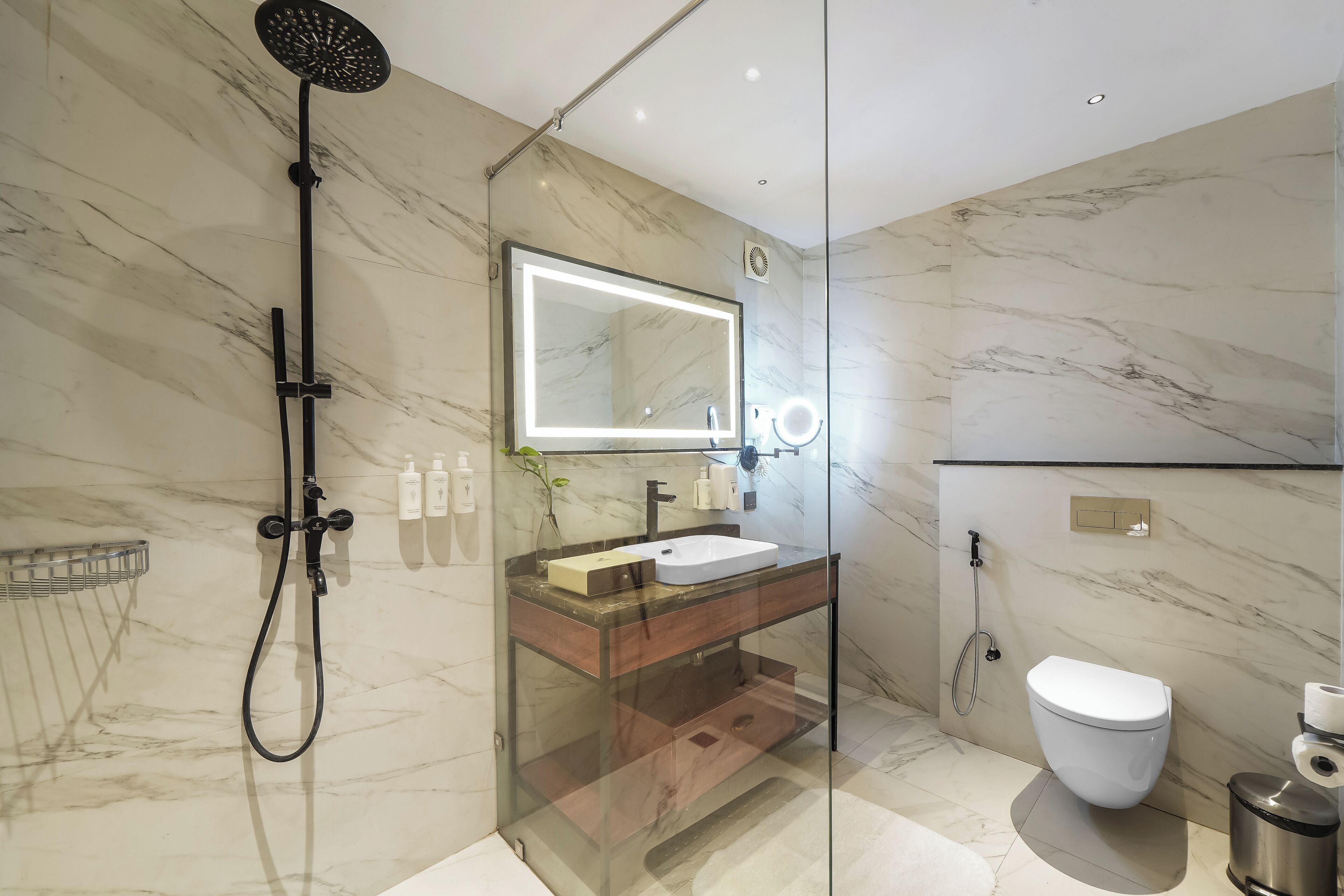 A modern bathroom with a glass-enclosed shower, a marble-tiled wall, a sink with a mirror, and a toilet.
